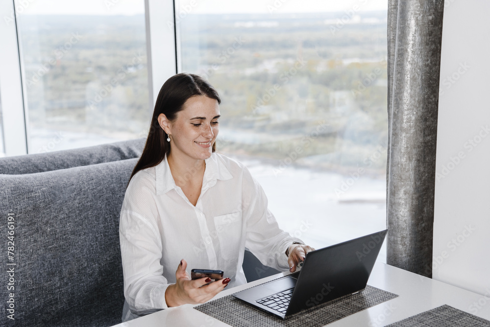 young focused freelancer working with notebook in cafe, typing text and smiling, smartphone in hand, concentrated caucasian businesswoman in white shirt, freelance concept young focused freelancer working with notebook in cafe, typing text and smiling, smartphone in hand, concentrated caucasian businesswoman in white shirt, freelance concept