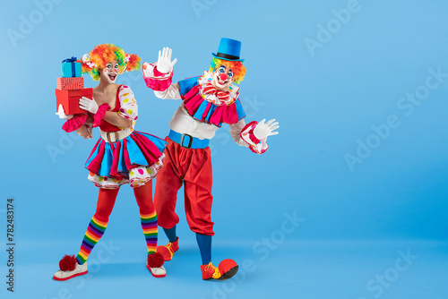 Funny female clown with gifts, man entertainer dressed as a colorful Joker in a suit and wig, with clown whiteface makeup. She is a trickster, jester, pantomime, mime, professional actor