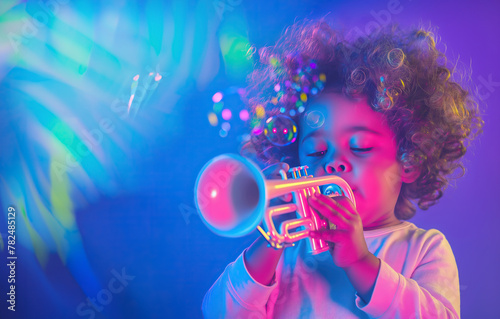 Little child boy musician with curly hair playing music with toy trumpet in blue and pink spotlights with bubbles and copy space on stage