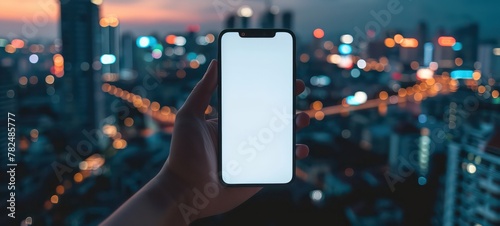 Hand holding smart phone with clean white blank screen mockup with city skyline defocused background for technology and app concepts