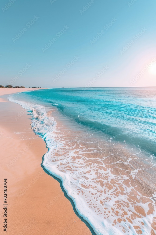 A serene image of a sandy beach with a gentle wave rolling in. The sky is a clear blue, and the sun is setting on the horizon.