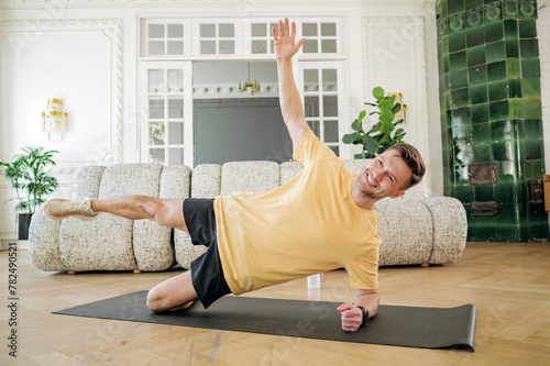 Man performing an advanced side plank exercise, demonstrating balance and core strength in a spacious living area. photo