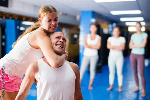 Determined young girl performing rear choke hold while sparring with male opponent during self defence training in gym