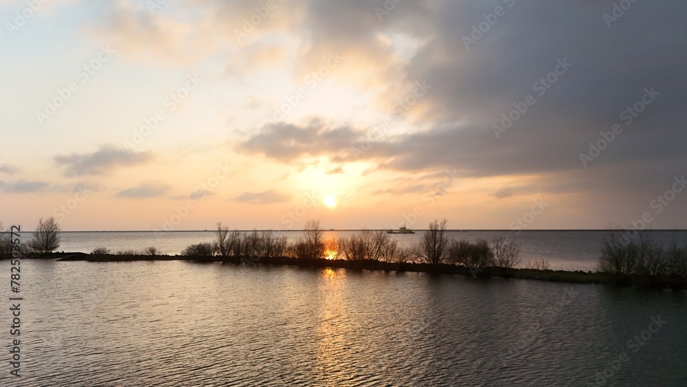 Serene sunset over a calm lake with silhouettes of distant trees and a small boat on the horizon under a soft gradient sky.