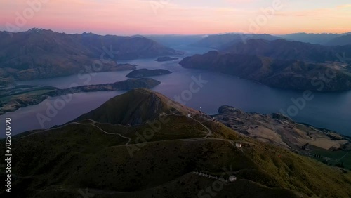 Aerial orbit of tourists on Roy's Peak viewpoint overlooking lake Wanaka during pink sunrise