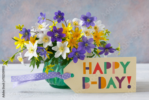 Bouquet of spring blue, purple, white and yellow flowers in a vase on the table and a card with the text happy birthday.
