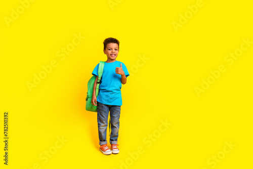 Full body photo of adorable small child dressed blue t-shirt jeans hold bag showing thumb up isolated on vibrant yellow background