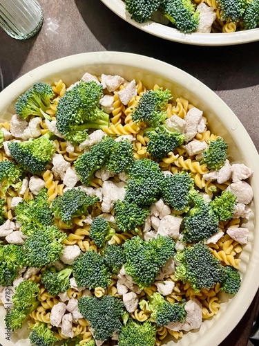 A ceramic baking dish with broccoli pasta and pieces of slightly fried chicken breast stands on the table in the kitchen.view from above . before baking process of cooking food at home. healthy eating