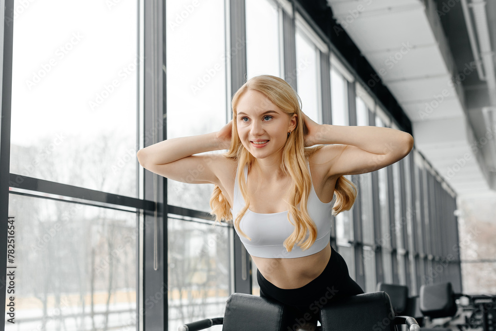 young athletic caucasian woman trains in fitness gym, doing hyperextension on exercise equipment, blond girl in white top and black leggings, healthy lifestyle concept young athletic caucasian woman trains in fitness gym, doing hyperextension on exercise equipment, blond girl in white top and black leggings, healthy lifestyle concept