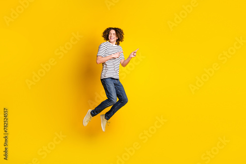 Full size portrait of nice young man jump point fingers empty space wear striped t-shirt isolated on yellow color background