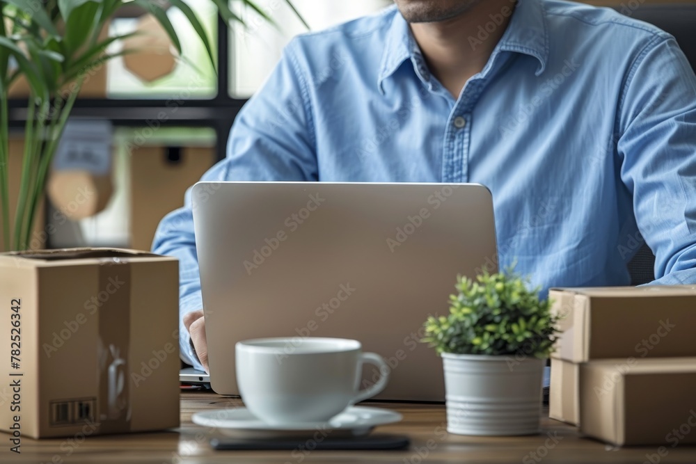 A close-up showcases a man's hand as he types on a laptop, with packages suggesting a home business setting