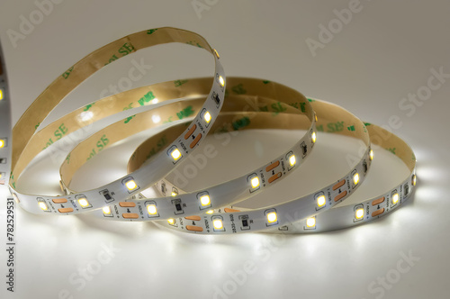 Illuminated led strip light coils on white background. White glowing led tape rolled up in circular shapes, displaying the flexible nature of modern lighting solutions.