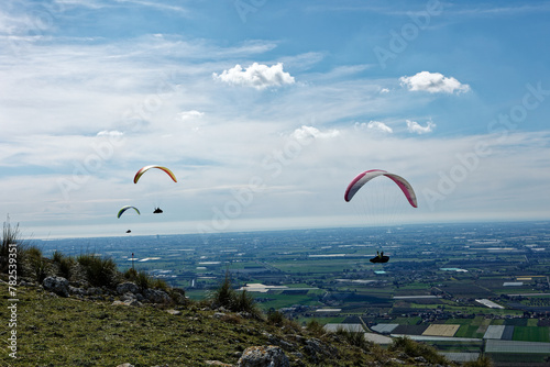 People enjoy the extreme sport of paragliding. Outdoor living in the blue sky. Incredible nature and views. Adventures and adrenaline with parachute. Travel destination Norma Latina Italy. Summer 