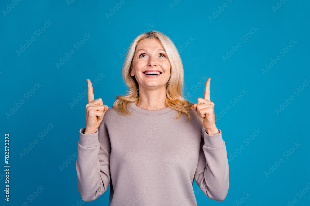 Photo portrait of lovely senior lady point look up empty space dressed stylish gray garment isolated on blue color background Photo portrait of lovely senior lady point look up empty space dressed stylish gray garment isolated on blue color background