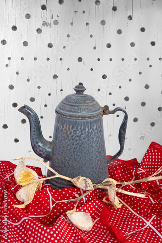 Tea coffee pot sits on red polkadot cloth with milk weeds as table decoration. Background shows star design of holes in old white seat board. Casual coffee break or meal is here. photo