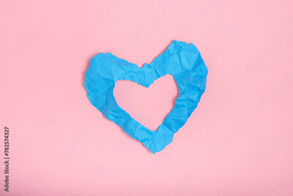 Blue crumpled paper texture in the shape of heart isolated on pink background. Concept of love, heartbreak.