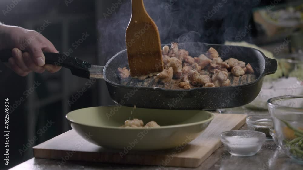 The cook places fried chicken from a black pan onto a plate in the restaurant kitchen, against a black backdrop. Close up. Slow motion. 4k The cook places fried chicken from a black pan onto a plate in the restaurant kitchen, against a black backdrop. Close up. Slow motion. 4k