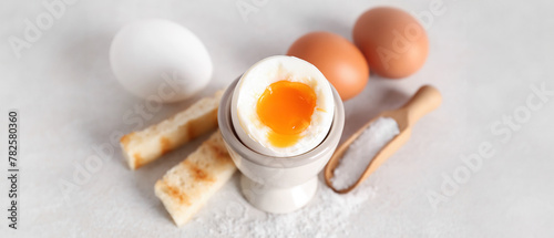 Holder with soft boiled egg, toasted bread and scoop on white table photo
