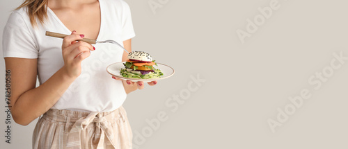 Young woman eating tasty salad on light background © Pixel-Shot