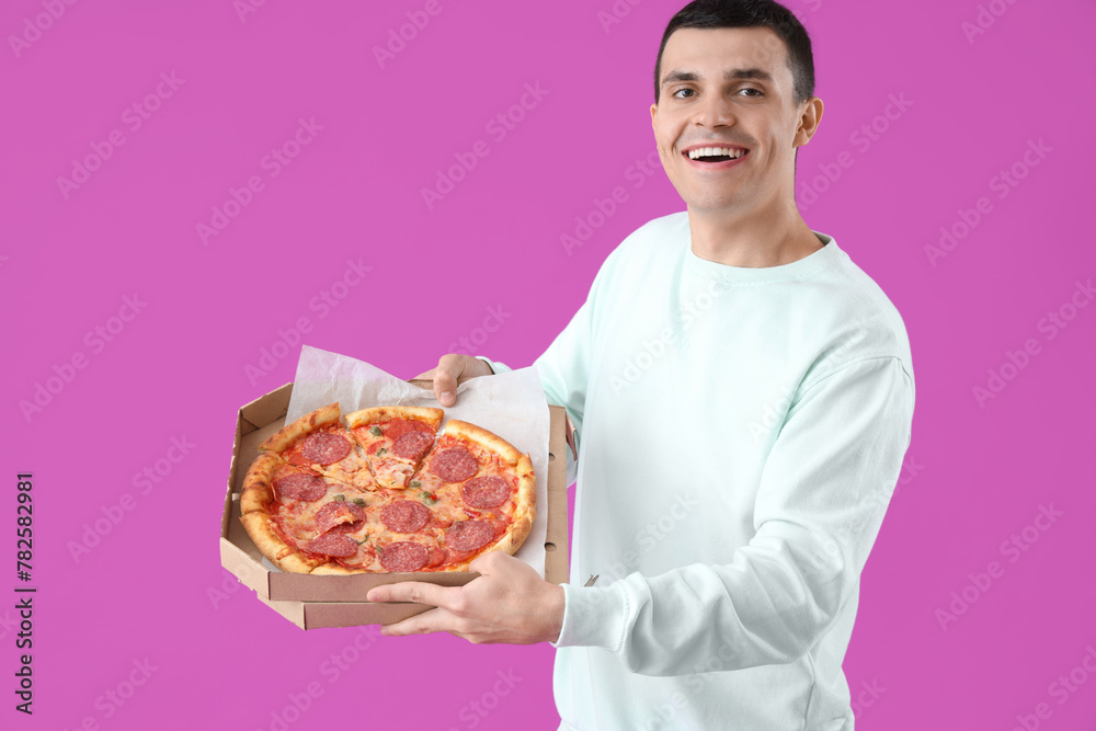 Young man with tasty pepperoni pizza on purple background