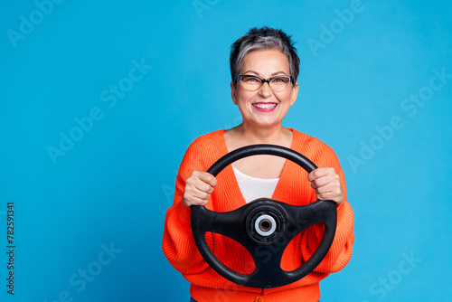 Photo portrait of lovely senior lady hold steering wheel dressed stylish orange garment isolated on blue color background
