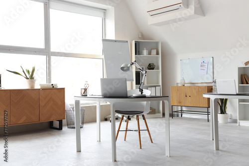 Interior of light office with shelving unit  chest of drawers  tables and chairs