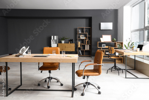 Interior of modern conference hall with wooden tables, shelving units and armchairs