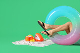 Young woman with inflatable ring, towel and headphones on green background. Summer holiday concept