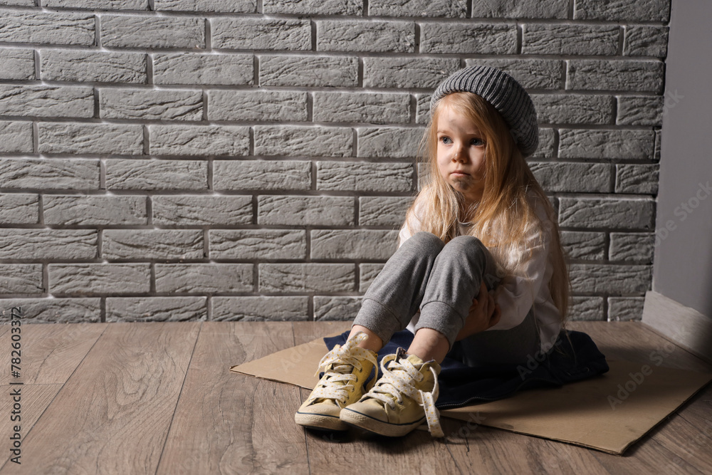 homeless little girl sitting on floor near grey brick wall - obrazy, fototapety, plakaty 