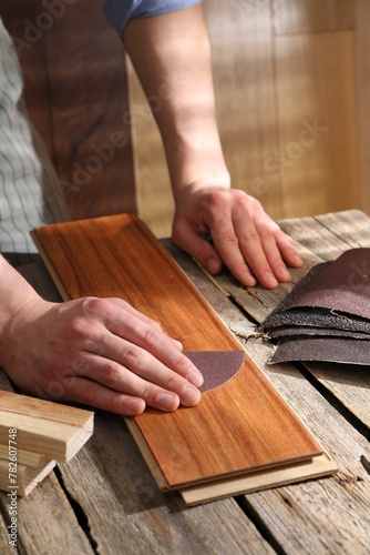 Man polishing wooden plank with sandpaper at table indoors, closeup