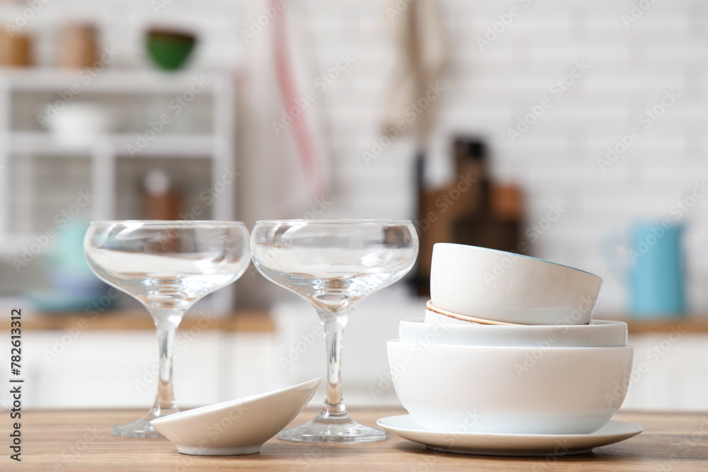 Stack of white clean tableware and glasses on wooden table in kitchen