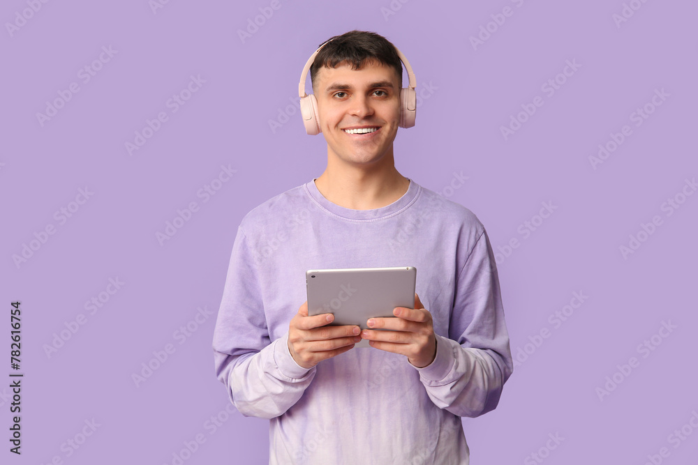 Handsome young happy man in headphones with tablet listening audiobook on purple background Handsome young happy man in headphones with tablet listening audiobook on purple background