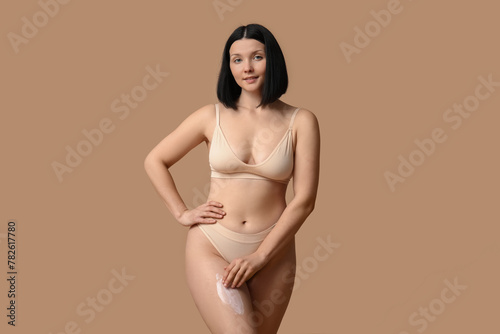Beautiful young happy woman with anti-cellulite cream on brown background