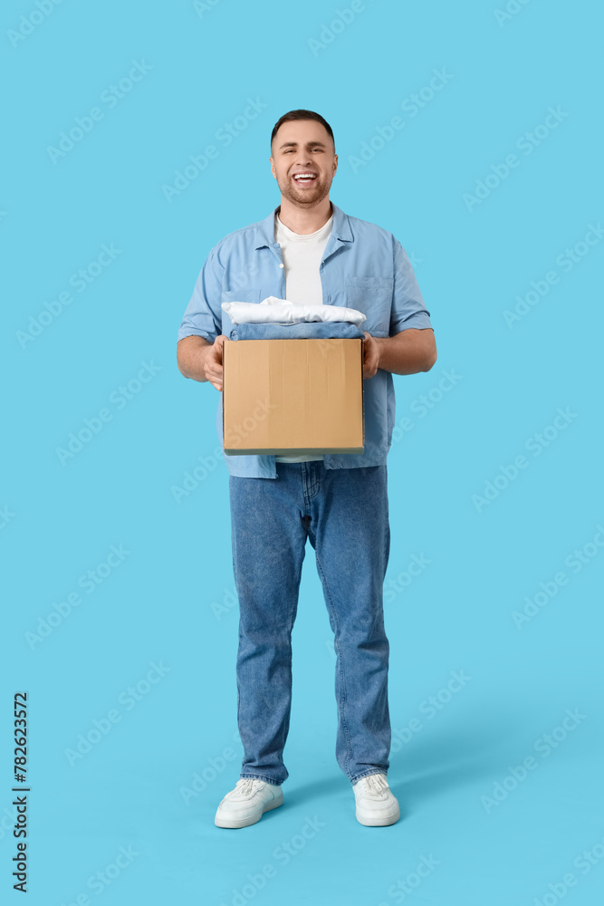 Young man holding box with clothes on blue background Young man holding box with clothes on blue background
