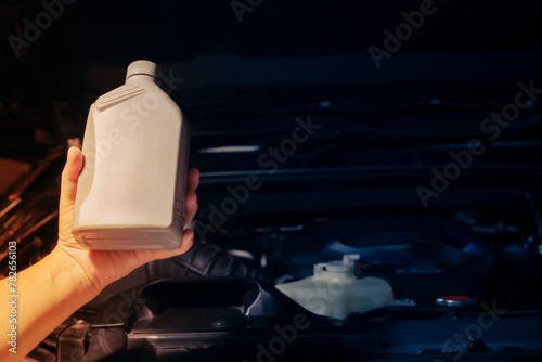 Auto mechanic holding a bottle of lubricant Engine background, oil change shop, engine service industry.