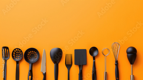 Variety of black kitchen utensils are neatly aligned on orange background, leaving ample copy space photo