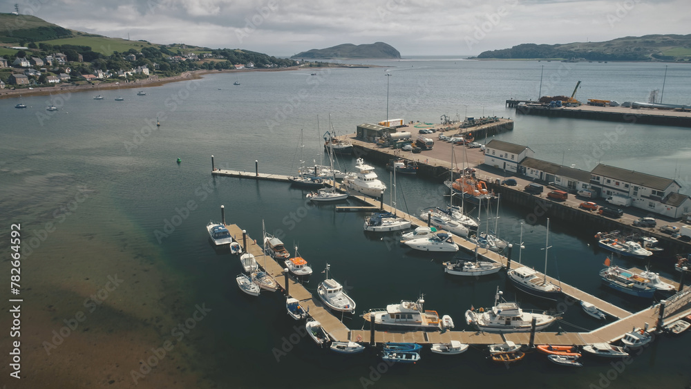 Sun pier seascape of marina with yachts, ships, boats on ocean bay aerial. Port cityscape with buildings at street near traffic road. Cars, trucks and vans drive on roadway. Cinematic summer landscape