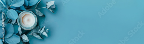 Open cream jar on blue background surrounded by navy leaves. Flat lay. Banner. Copy space.