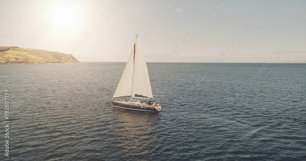 Sun at ocean bay with luxury yacht aerial. Nobody nature seascape at sunlight summer cruise. Sail boat at open sea. White sailing ship on water at cinematic drone shot. Travel and tourism concept