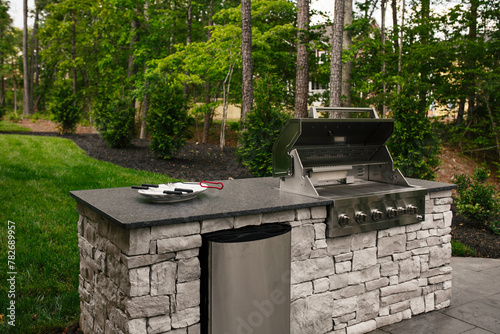 Modern Stainless Steel Grill Built Into a Stone Countertop with A Backyard Lawn © Bryan