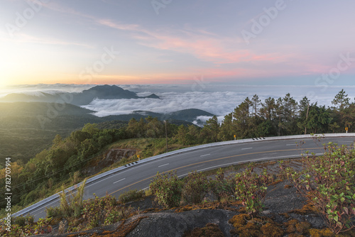 Long curvy forest asphalt road over the hills. Beautiful curved road in the forest. Side view of road with fog at sunrise.