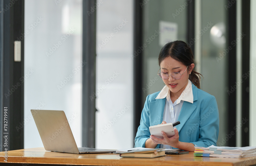 Asian businesswoman in glasses smiles at the concept of working with a calculator to calculate business income in finance, online, taxes on laptop at office. Asian businesswoman in glasses smiles at the concept of working with a calculator to calculate business income in finance, online, taxes on laptop at office.