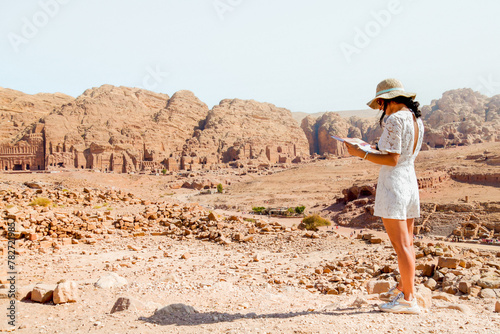 Fashionable caucasian woman tourist, read map, plan exploring the sights of the ancient, fabulous city of Petra in Jordan. Colorful photos. Concept of leisure, vacation and travel