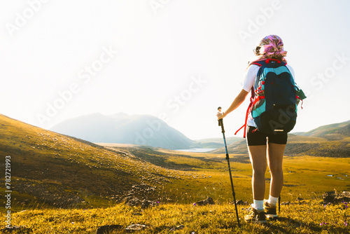Young caucasian girl hiker stands on viewpoint against the backdrop of mountains and watches the sunset