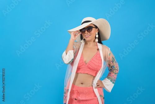 Woman wearing beach outfit and sunglasses with positive attitude. Studio portrait, blue background.