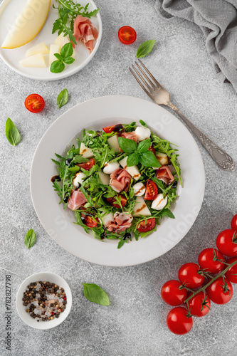 Fresh summer salad with arugula, melon, prosciutto and mozzarella cheese on concrete background, Healthy food. Top view.