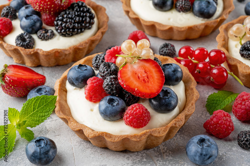 Tartlets with custard vanilla cream with fresh berries and mint on a gray concrete background. Summer dessert.