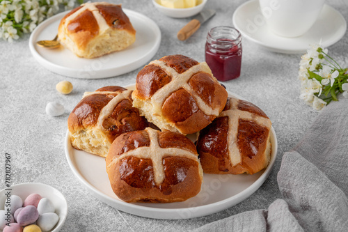 Traditional Easter hot cross buns on a white plate with butter, berry jam and cup of tea. Delicious Easter breakfast.