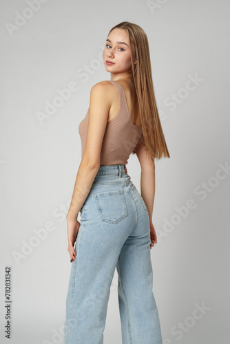 Young Woman Wearing High Rise Jeans and Tank Top posing on gray background in studio
