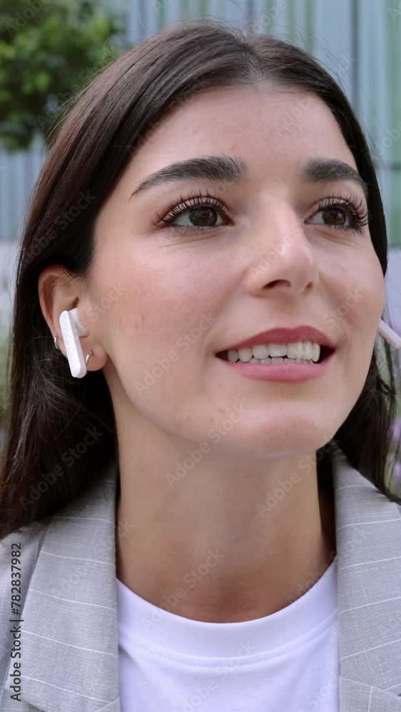 Vertical 9:16 video. Young business woman talking on the cellphone using wireless earphones while sitting at outdoor area of office building center. Technology and business concept. Vertical 9:16 video. Young business woman talking on the cellphone using wireless earphones while sitting at outdoor area of office building center. Technology and business concept.